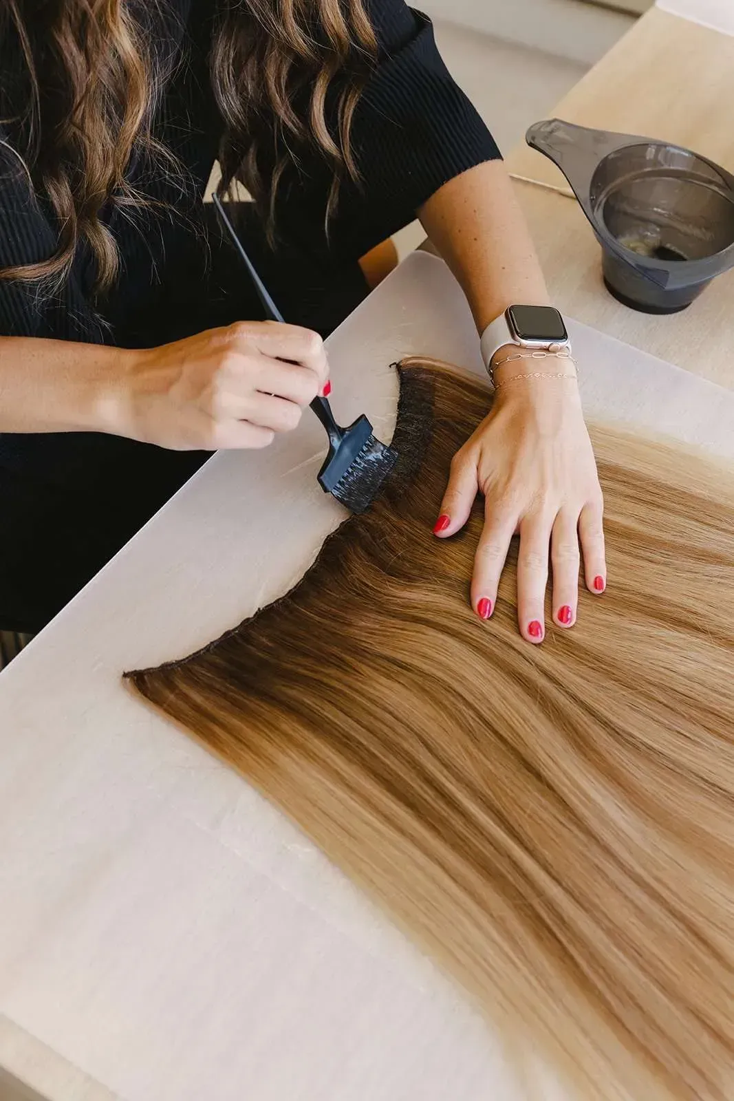 A woman is sitting at a table painting her hair with a brush.