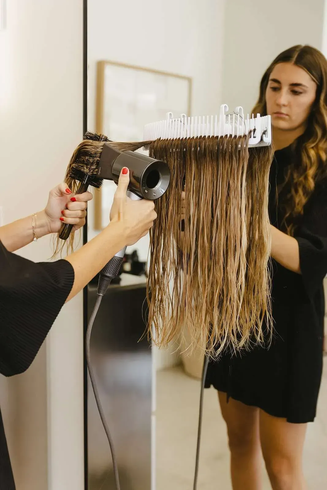 A woman is getting her hair blow dried by a hairdresser in front of a mirror.
