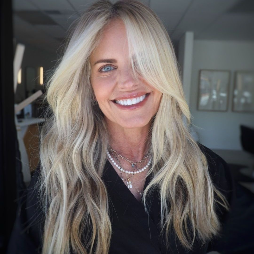 Woman with long blonde hair, smiling, wearing a necklace.